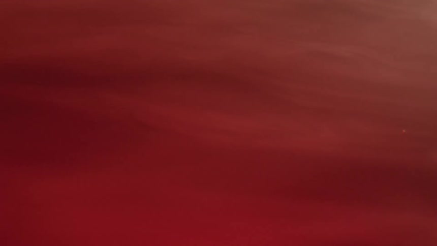 A surface with a deep red color with subtle variations in tone from light to dark from smoke billowing over it