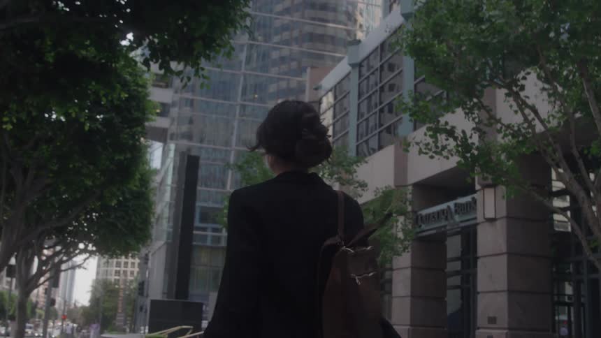 Close up of a young woman walking away on a metropolitan city sidewalk during daytime