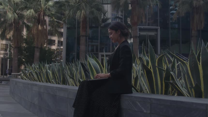 The woman types on her laptop outside the building