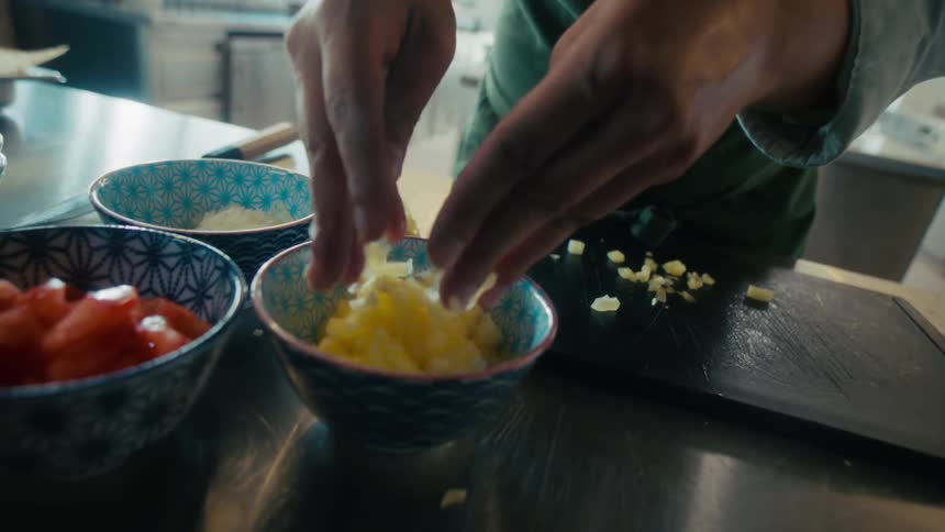 Hands place chopped food into a bowl in a kitchen setting