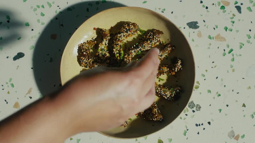 A persons hand sprinkles spices on a plate of eggplant