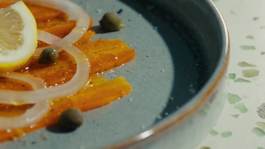 Thin slices of carrot arranged on a plate with onions lemon and capers