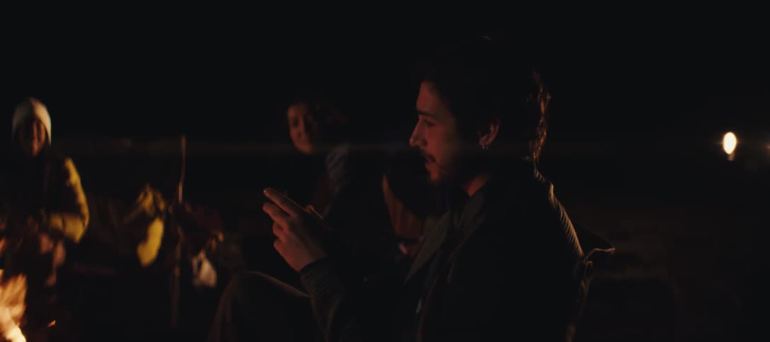 Three people sitting around a campfire at night