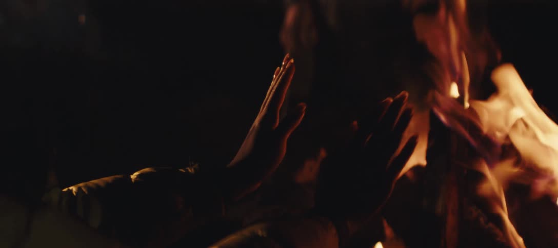 A woman warms her hands by the campfire
