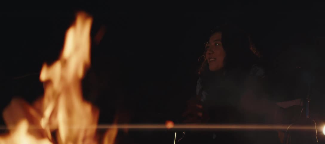 Friends sit by a campfire at night smiling and talking