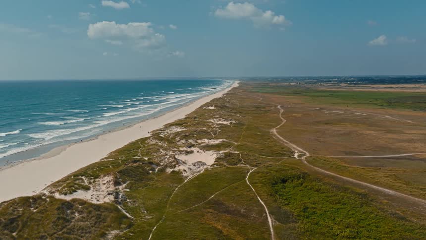 Aerial view of a long stretch of beach with blue sea next to dunes and coastal vegetation