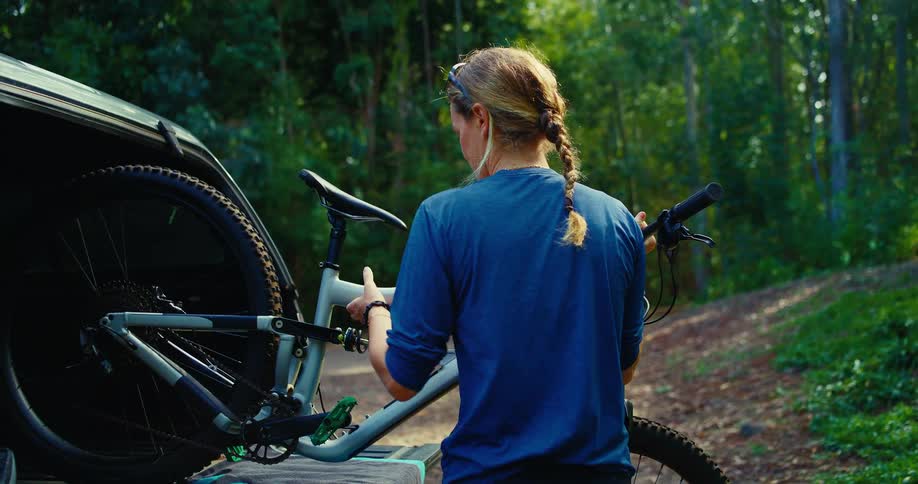 The woman removes the bike from the vehicle in the woods