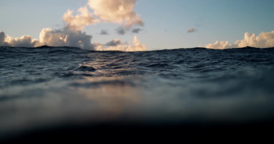 Waves move across the ocean beneath dramatic sunset clouds