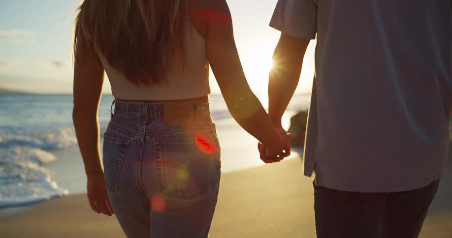 A couple hold hands while walking on the beach