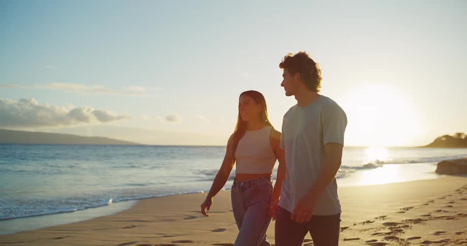 A couple walks hand in hand along the beach at sunset