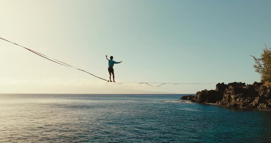 Person walking on a slackline stretched over the sea balancing with arms open