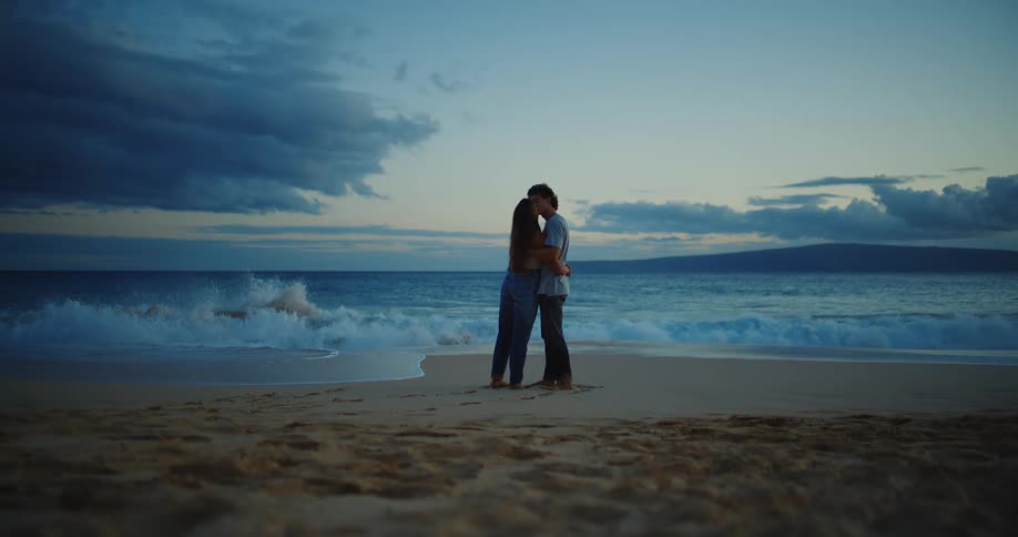 A young couple fully dressed on a beach standing by the water hugging and kissing