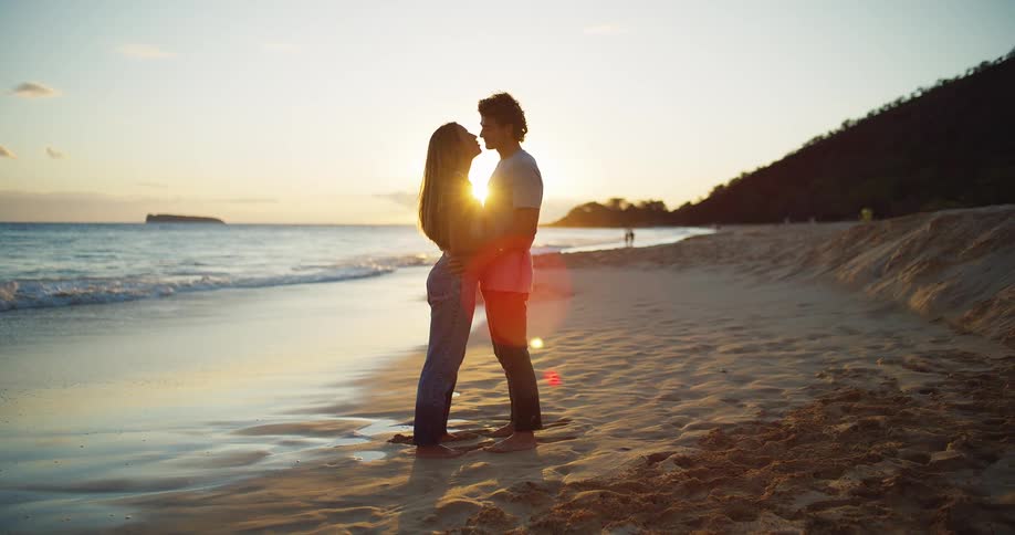 Young couple kissing and hugging next to the ocean on the sand at sunset