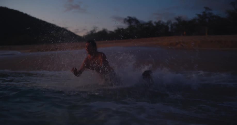 Couple holding hands runs through the surf and dives into the water in the evening