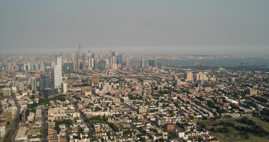 Aerial view of a large city by a bay with skyscrapers and a hazy gray sky in the background