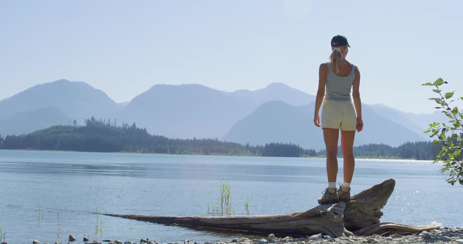 The woman stands on driftwood by the lake shore