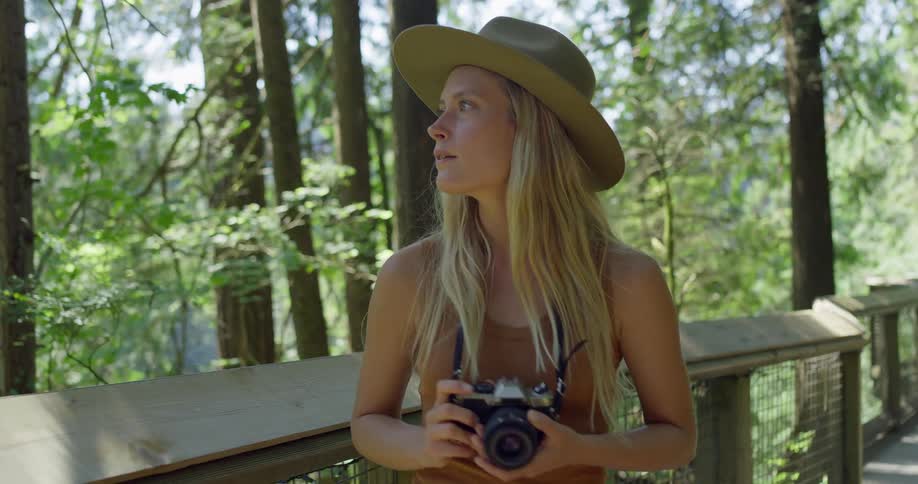 The woman is holding her camera as she walks through the woods