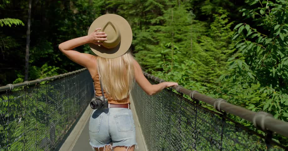 A woman walks across a suspension bridge in a forest