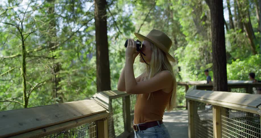 The woman is snapping shots of the forest as she walks