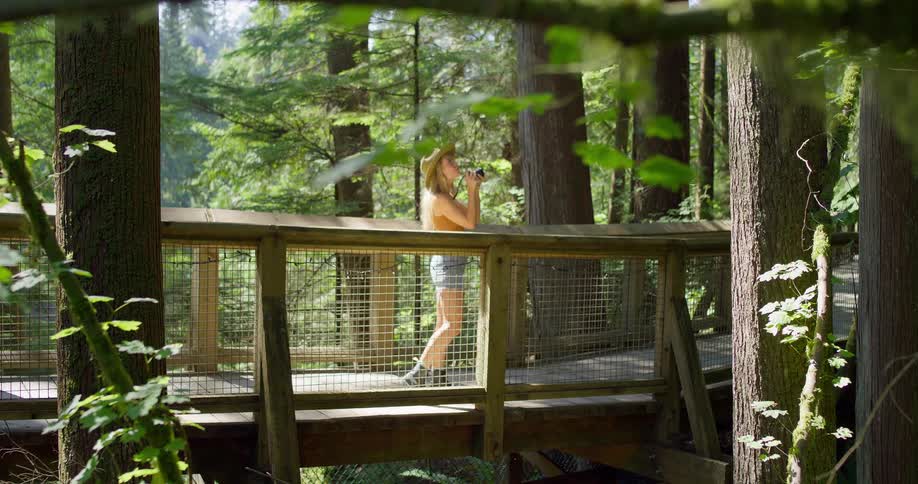 The woman walks on the small bridge and takes photos of the forest