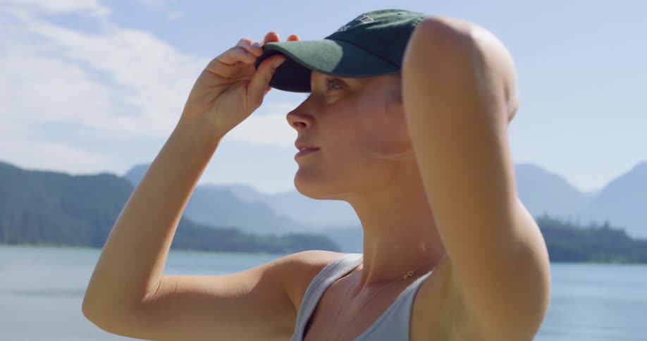 Woman adjusts her cap while enjoying the lakeside scenery
