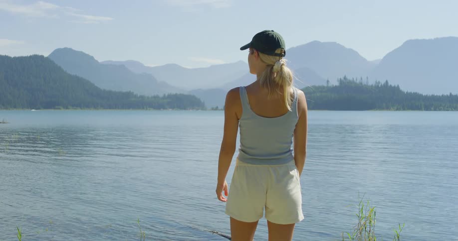 A woman walks to the edge of a lake in the mountains