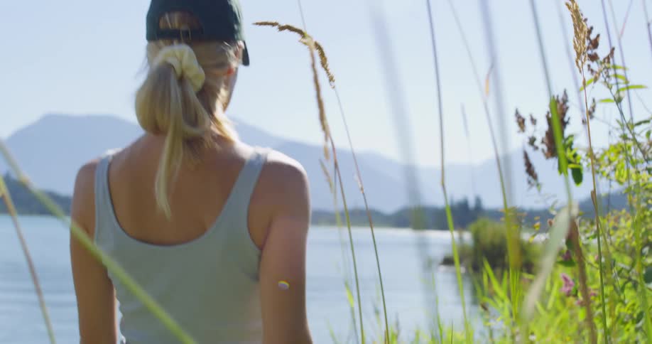 A woman hikes through some tall grass at the edge of a lake