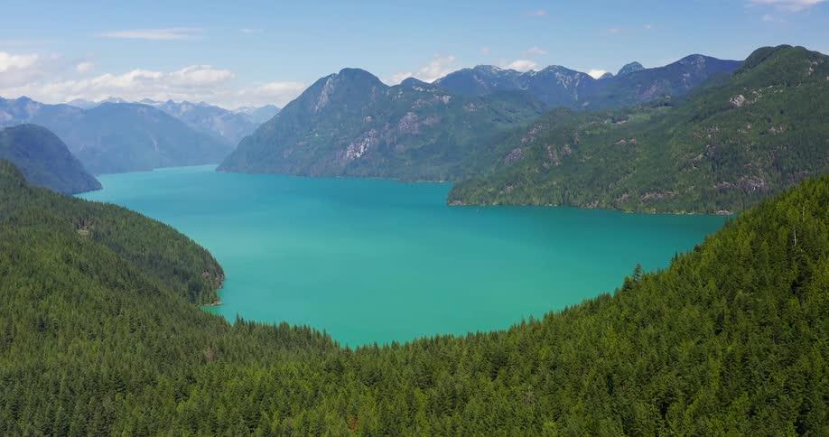 Forested mountains surround a lake under a cloudy sky