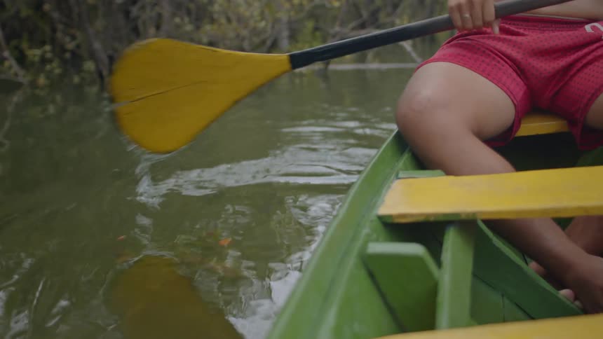 The man is paddling a rowboat in the swamp