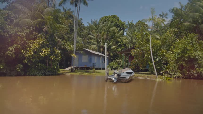 Stilted homes and a moored skiff line a brown river in a tropical settlement