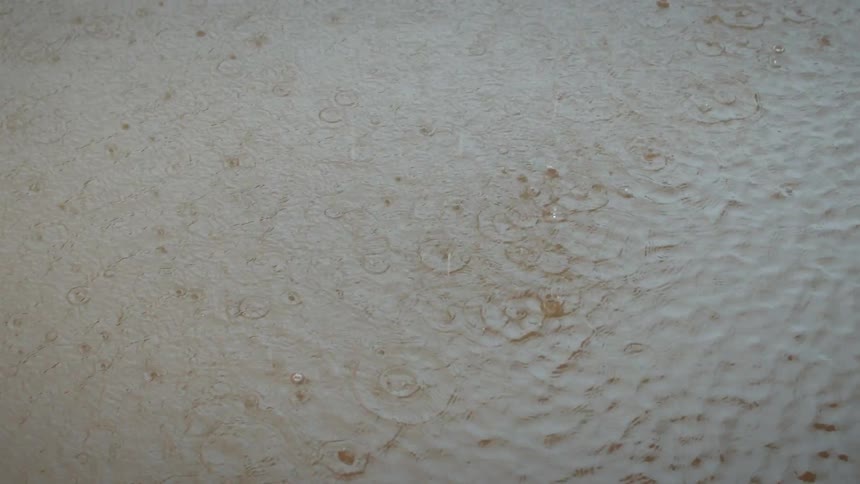 A topdown shot captures heavy raindrops splashing and creating ripples on the surface of a murky puddle during a storm