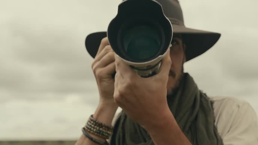 A man wearing a hat and scarf raises a camera to take a picture
