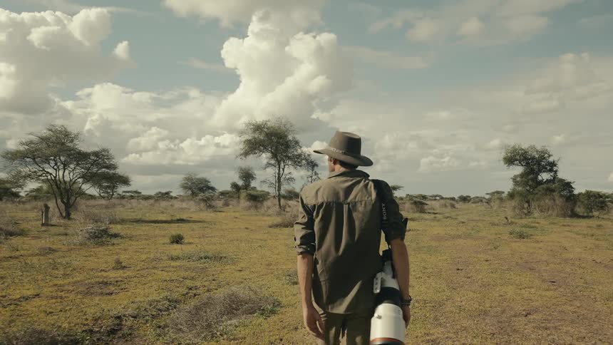 Man walking in a savanna with a camera hanging on his shoulder