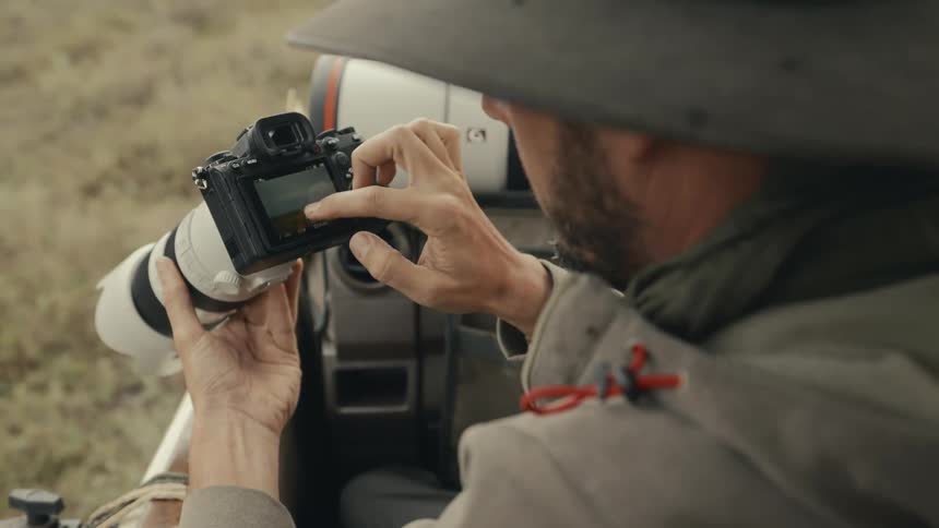 A travel shooter checks images on the camera screen from a safari vehicle