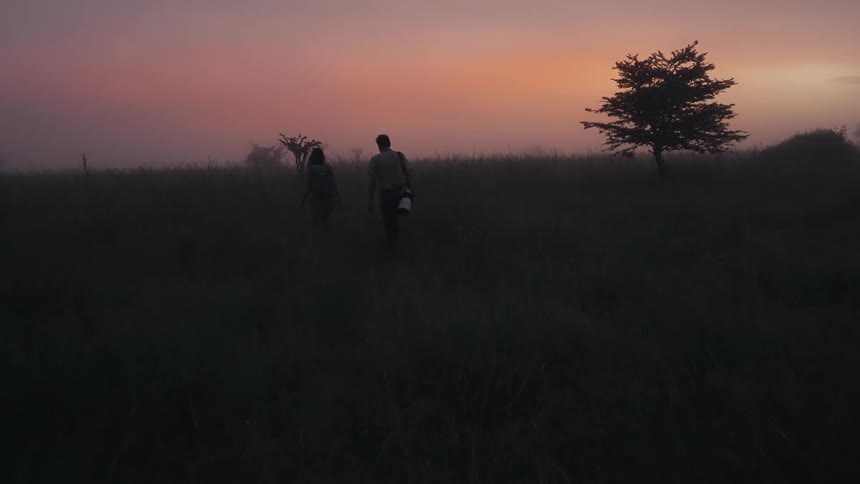 A man carries a camera as he walks through a field with a woman