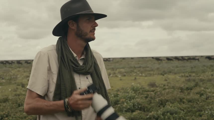 A photographer walking across a grassy field stops to take a photograph with a camera
