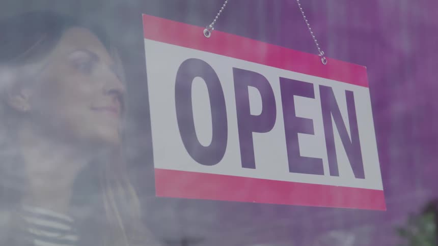 The woman turns the sign to open on the shop window