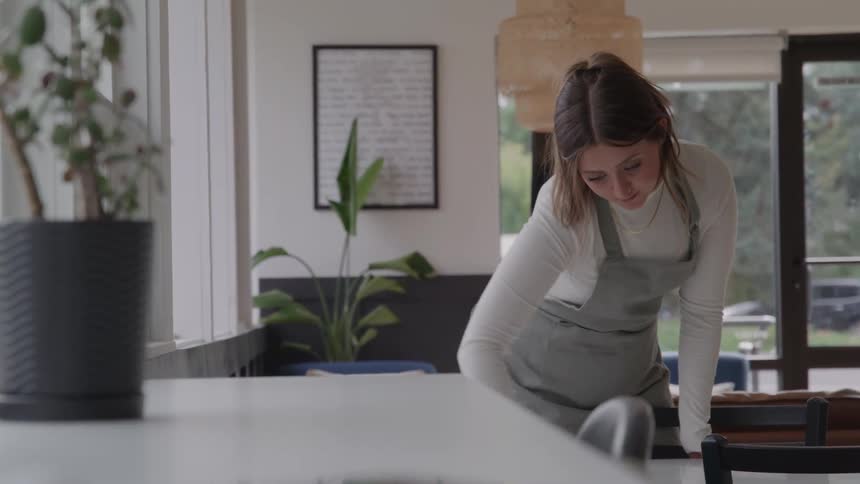 A female worker leans forward as she wipes down a table