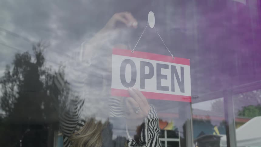 A young restaurant worker walks to the front door and changes the sign from closed to open at midday
