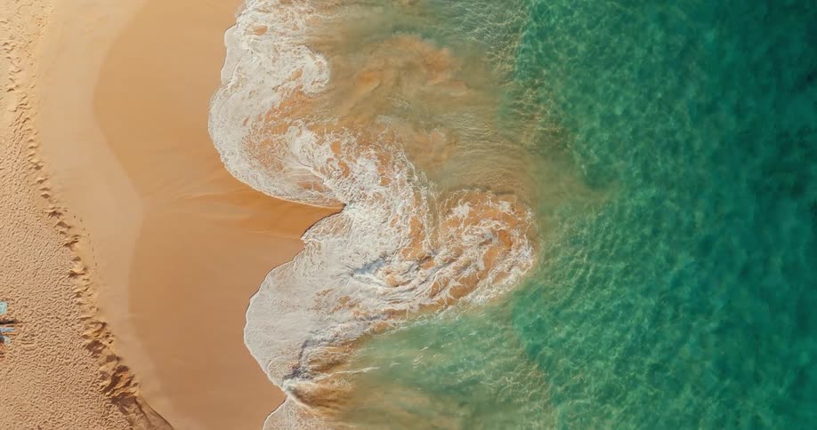 Small waves breaking on a sandy beach causing waves to return back to the sea