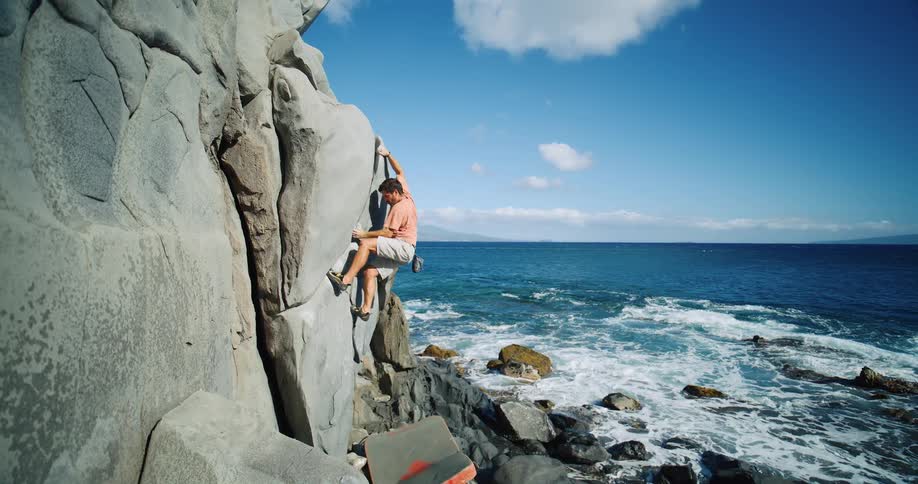 A man mountain climbs a rocky cliff above the ocean