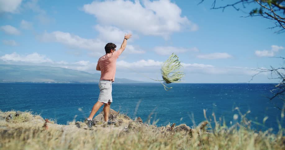 A man using a rope to throw himself forward on a cliff facing a blue sea