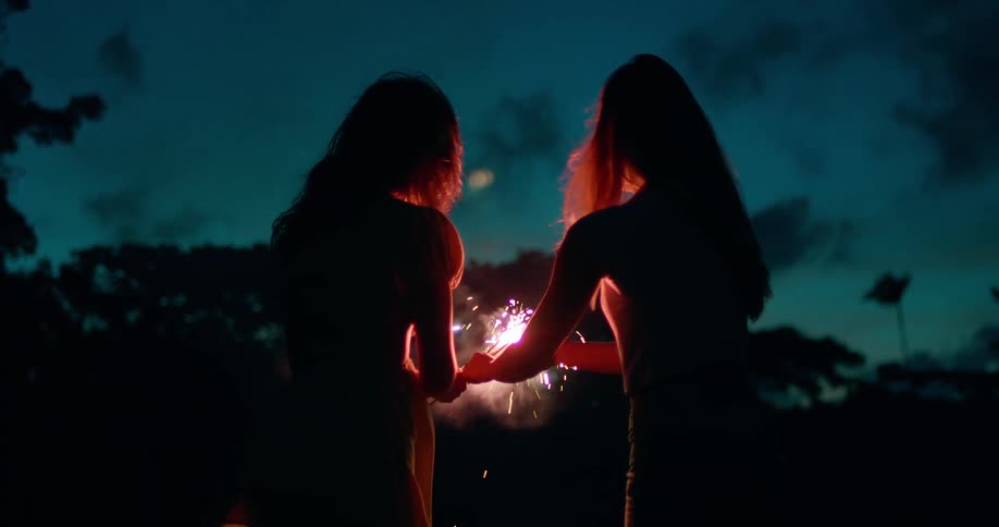 Two women hold sparklers at dusk while celebrating outdoors