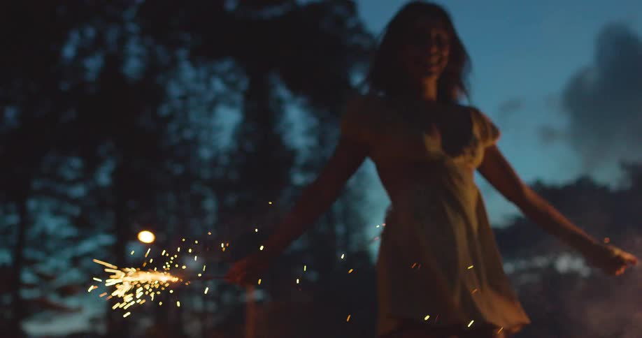 The video shows a woman joyfully dancing at dusk holding sparklers that illuminate the scene