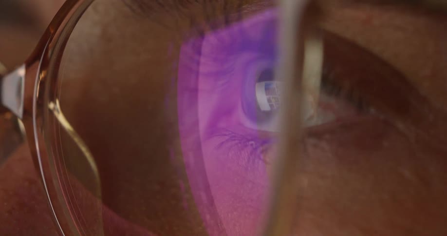 A persons eye wearing glasses with a reflection of a computer screen visible on the lenses