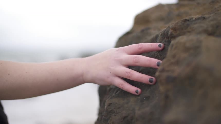Person glides their hand against a large rock while they walk