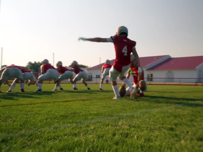 American football player kicking the ball during practice with the team lined up on the field