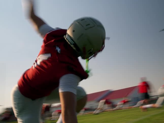 A blurry video shows an american football player in a red and white uniform on the field the player is in a crouched position ready to run