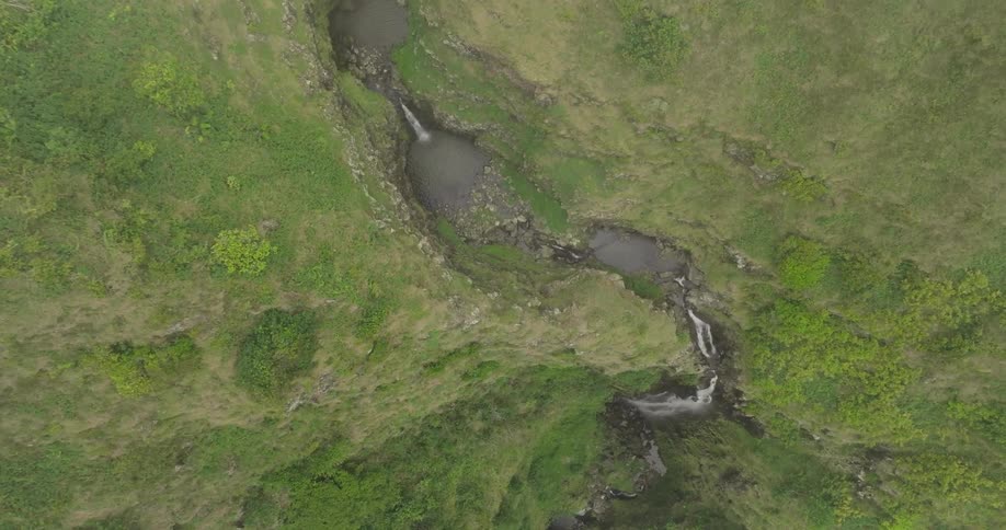 An aerial shot captures a series of small waterfalls and pools nestled within a lush green landscape the camera slowly descends to reveal the full view of the cascades