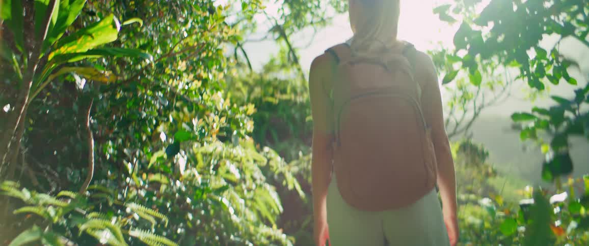 A young woman carrying a backpack hiking in the woods at midday